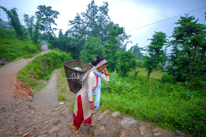 Asha, a clothes shop owner in Ilam District, carries a gagri full of water back to her home.